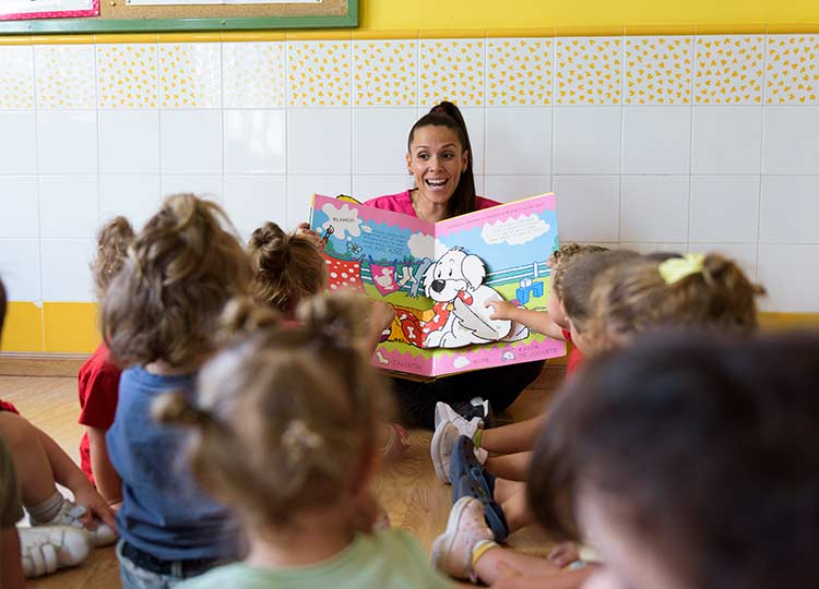 Educadora de la escuela infantil mostrando un libro a los alumnos