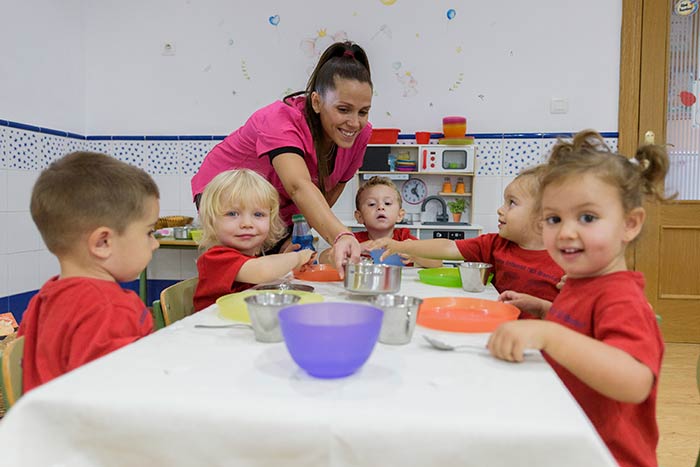 Los niños de la escuela infantil junto a una educadora preparados para comer