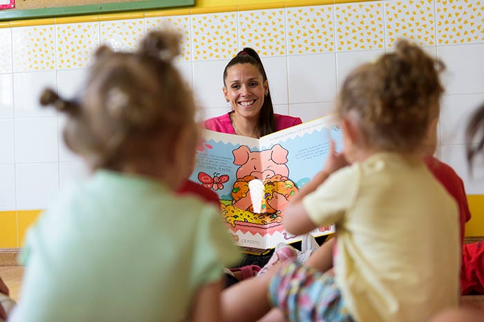 Profesora mostrando un libro de cuentos a los alumnos de la escuela infantil